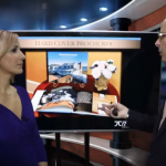 Man talking with woman with large screen behind them about brochures and listing tools