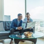 Expertise, Confidence, and Collaboration in Luxury Real Estate. Two professionals reviewing documents together in an office with a cityscape in the background.