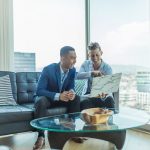 Expertise, Confidence, and Collaboration in Luxury Real Estate. Two professionals reviewing documents together in an office with a cityscape in the background.