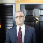 Man in business suite beside American flag.